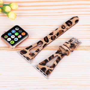 May include: Two leopard print Apple Watch bands with a cutout design. The bands are brown and tan with black spots. The bands are shown on a light wood surface.