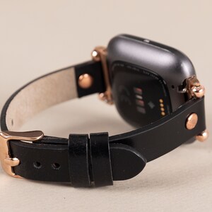 May include: A black leather watch band with rose gold accents and a black smartwatch with a screen displaying a heart rate.