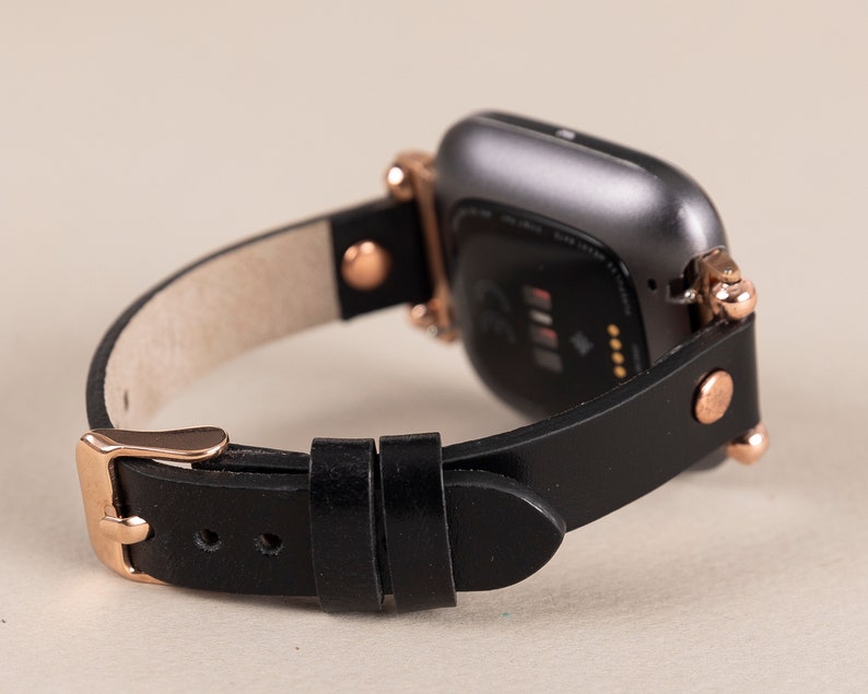 May include: A black leather watch band with rose gold accents and a black smartwatch with a screen displaying a heart rate.