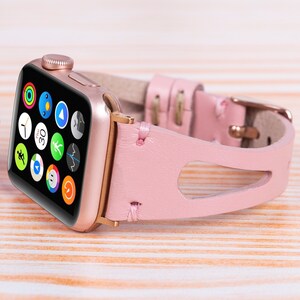 Peut inclure: Un bracelet de montre en cuir rose avec une Apple Watch dor&eacute;e. Le cadran de la montre affiche une vari&eacute;t&eacute; d'applications, y compris une minuterie r&eacute;gl&eacute;e sur 30 secondes.