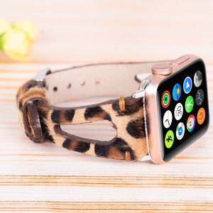 May include: A rose gold Apple Watch with a leopard print leather band. The watch face displays a variety of app icons.
