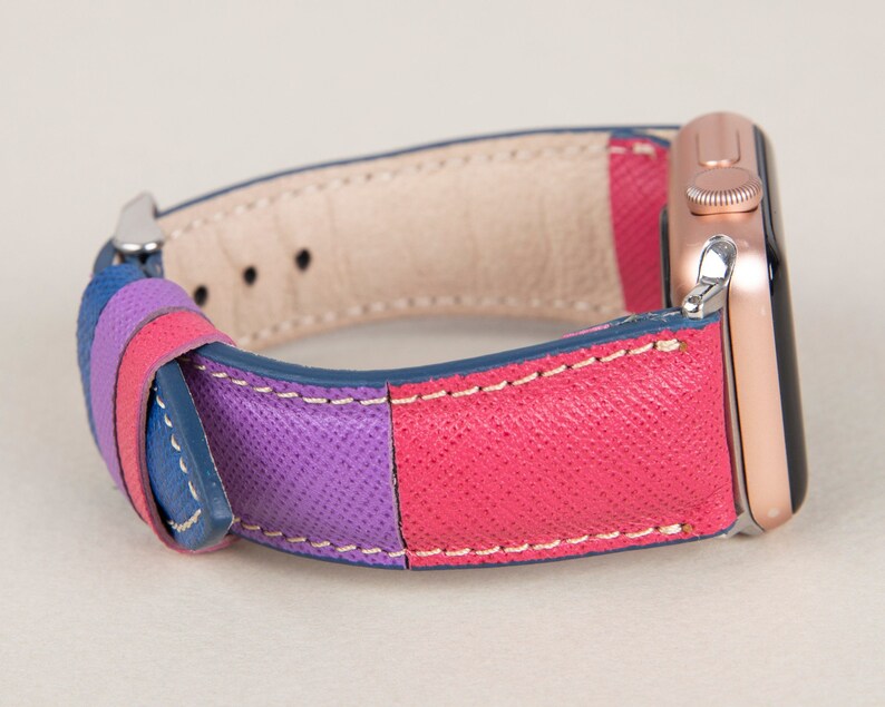 Puede incluir: Una correa de reloj de cuero colorida con rayas azules, moradas y rosas. La correa est&aacute; unida a un Apple Watch de oro rosa.