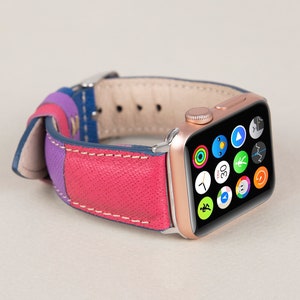 May include: A rose gold Apple Watch with a multi-coloured leather band. The watch face displays a variety of app icons, including a clock, compass, and music player.