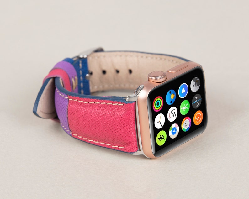Puede incluir: Un Apple Watch de oro rosa con una banda de cuero multicolor. La esfera del reloj muestra una variedad de iconos de aplicaciones, incluyendo un reloj, una br&uacute;jula y un reproductor de m&uacute;sica.