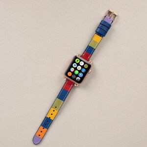 K&ouml;nnte beinhalten: Ein farbenfrohes Apple Watch Armband mit einem gestreiften Muster in Blau, Rot, Gelb und Gr&uuml;n. Das Armband ist aus Leder und hat eine ros&eacute;goldene Schlie&szlig;e.