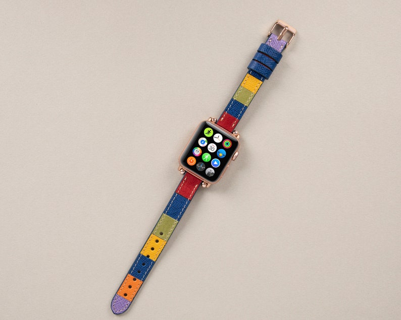 K&ouml;nnte beinhalten: Ein farbenfrohes Apple Watch Armband mit einem gestreiften Muster in Blau, Rot, Gelb und Gr&uuml;n. Das Armband ist aus Leder und hat eine ros&eacute;goldene Schlie&szlig;e.