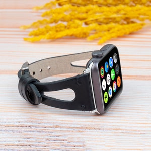 Könnte beinhalten: Ein schwarzes Lederarmband mit einer silbernen Schnalle und Aussparungen. Das Armband ist an einer silbernen Apple Watch mit einem schwarzen Bildschirm befestigt, auf dem verschiedene App-Symbole angezeigt werden.