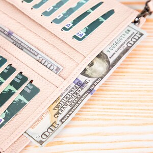 Pu&ograve; includere: Un portafoglio color rosa chiaro testurizzato con molteplici fessure verticali per carte e due scomparti interni contenenti diverse banconote da cento dollari americani. Il portafoglio presenta una finitura granulata e una cerniera.