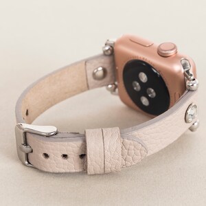 Pode incluir: Uma pulseira de rel&oacute;gio Apple de couro cinza claro com strass e um mostrador dourado.