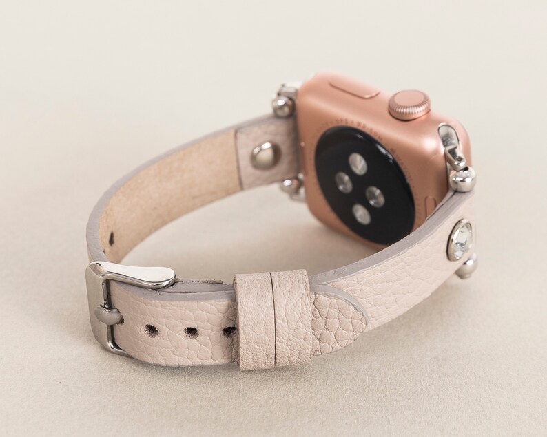 Pode incluir: Uma pulseira de rel&oacute;gio Apple de couro cinza claro com strass e um mostrador dourado.