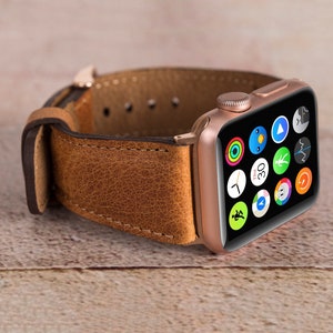 May include: A rose gold Apple Watch with a brown leather strap. The watch face shows a variety of app icons, including a clock, a compass, and a heart rate monitor.