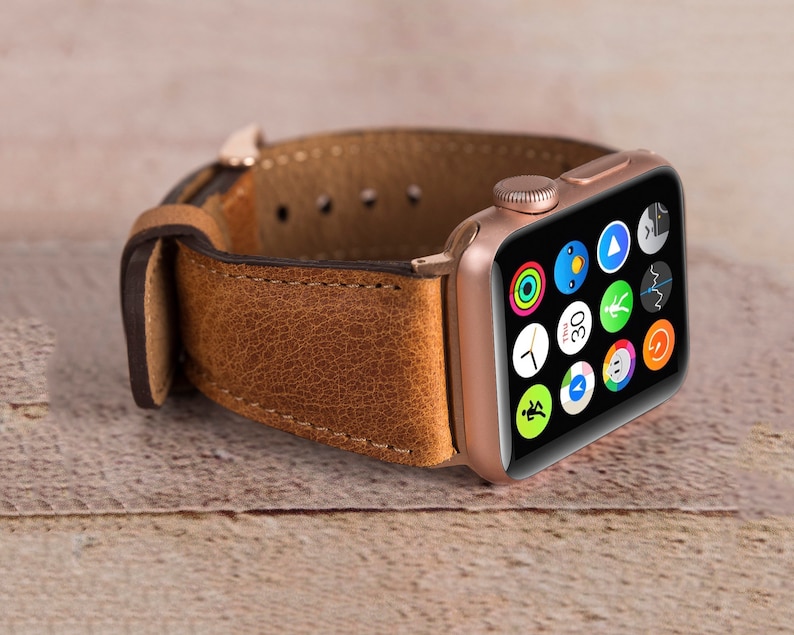 May include: A rose gold Apple Watch with a brown leather strap. The watch face shows a variety of app icons, including a clock, a compass, and a heart rate monitor.