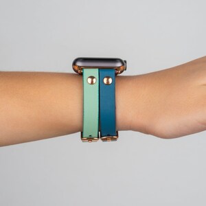May include: A smartwatch with a teal and light green leather band. The band has gold accents and a rose gold buckle.