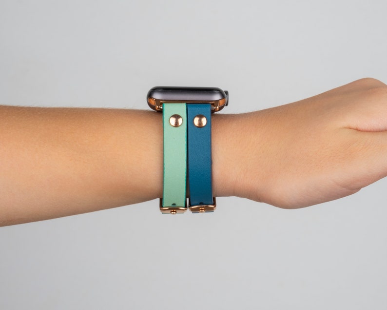 May include: A smartwatch with a teal and light green leather band. The band has gold accents and a rose gold buckle.