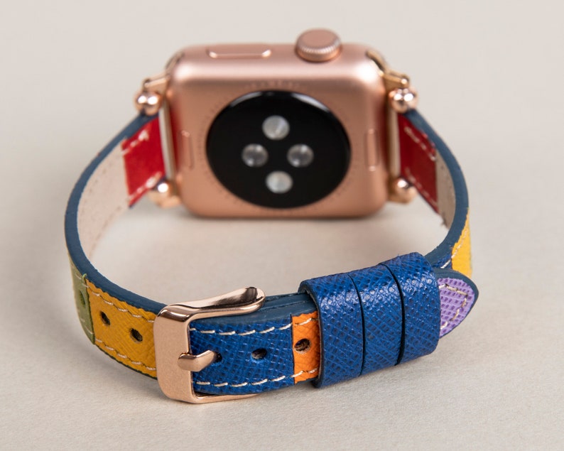 K&ouml;nnte beinhalten: Eine ros&eacute;goldene Apple Watch mit einem mehrfarbigen Lederarmband. Das Armband hat Streifen in Rot, Gelb, Gr&uuml;n, Blau und Lila.