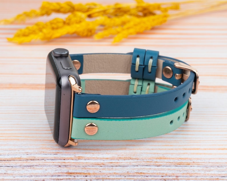 May include: A teal and light green leather Apple Watch band with rose gold accents and a buckle closure.