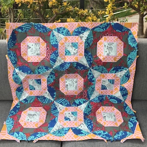 Peut inclure: Une courtepointe avec un motif géométrique dans des tons de bleu, rose et vert. La courtepointe est composée de carrés et de cercles, et le tissu a un imprimé floral.