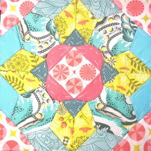 May include: A colourful patchwork quilt block with a pink, white and yellow centre surrounded by blue, green and yellow fabric squares.