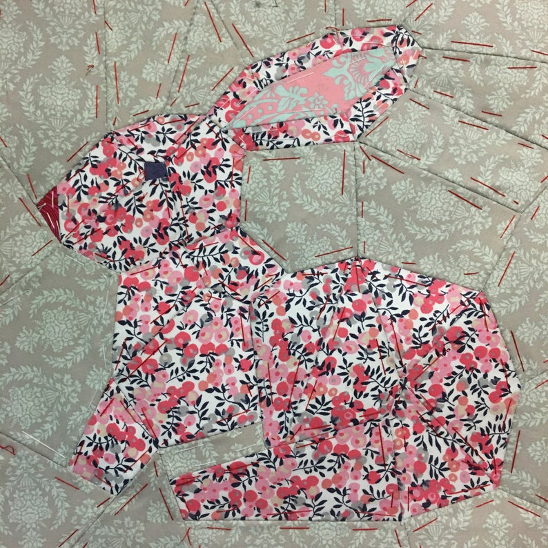 May include: A patchwork quilt block featuring a pink and white floral fabric design in the shape of a rabbit. The rabbit is surrounded by a gray fabric with a leaf pattern.