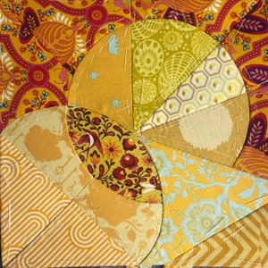 Peut inclure: Un bloc de courtepointe composé de différents tissus jaunes, orange et rouges avec des motifs floraux et géométriques. Le bloc est composé de pièces courbes cousues ensemble pour créer un motif en spirale.