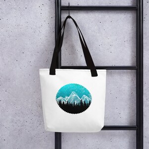 May include: White tote bag with black handles featuring a circular design of a blue and white mountain range with a starry sky background.