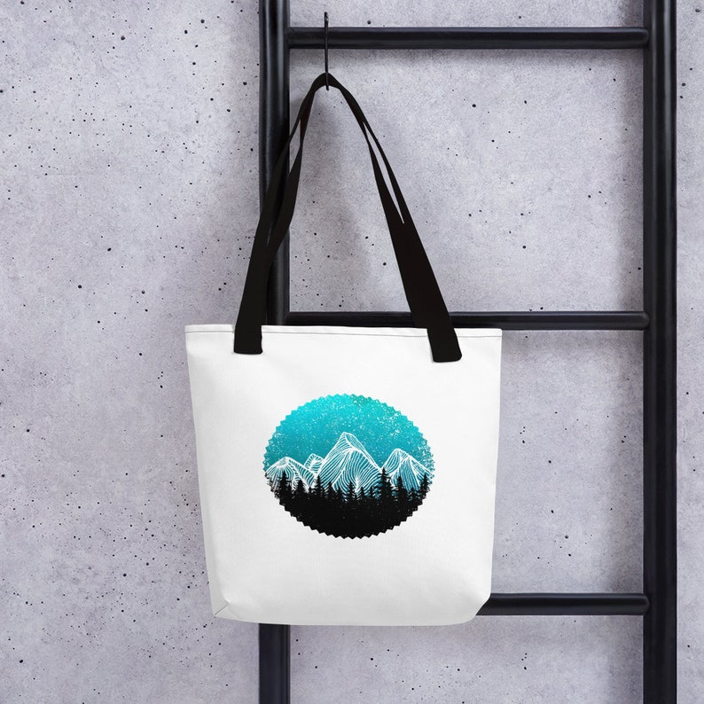 May include: White tote bag with black handles featuring a circular design of a blue and white mountain range with a starry sky background.