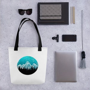 May include: White tote bag with black handles featuring a blue and white mountain range design in a circle. The design has a white outline and a black silhouette of trees at the base of the mountains.