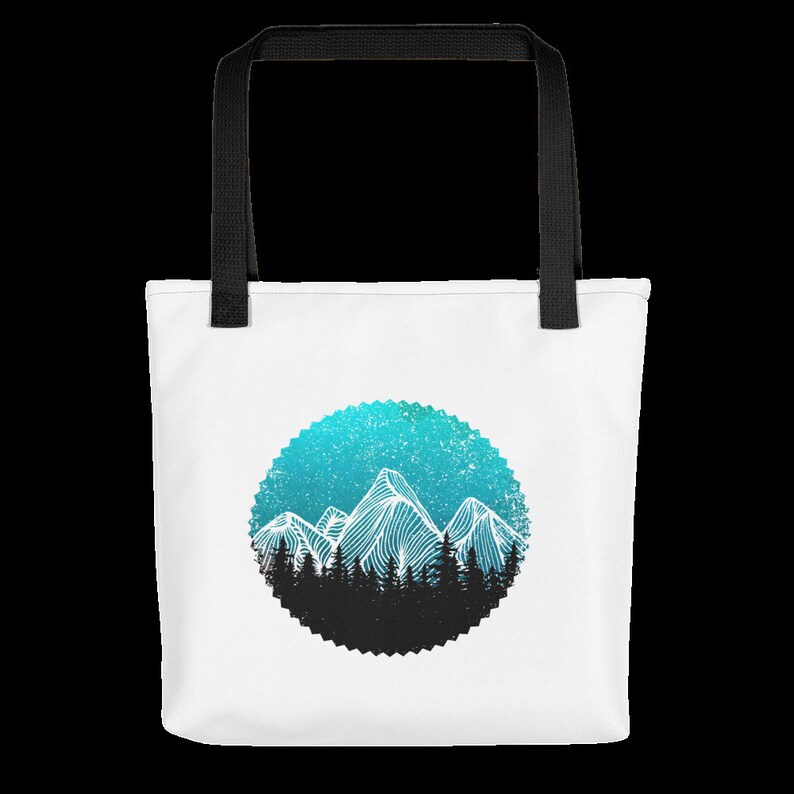 May include: White tote bag with black handles featuring a blue and white mountain range design in a circle with a black silhouette of trees at the base.