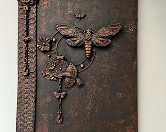 May include: A dark brown, textured wall art piece with a steampunk aesthetic. It features a large, detailed moth, clockwork elements, and a decorative border with chains and hooks. The artwork is approximately 61 cm tall and 46 cm wide.