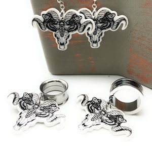 Pode incluir: Um par de brincos de prata com um design de caveira e borboleta em preto e branco. Os brincos são mostrados ao lado de duas expansores de orelha de prata com o mesmo design.