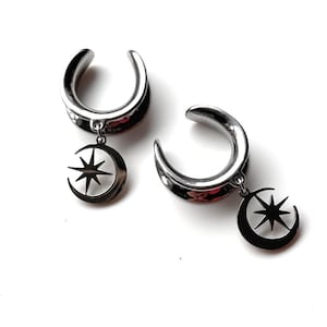 Può includere: Un paio di dilatatori per orecchie argentati con un ciondolo a forma di luna crescente e stella. I dilatatori hanno un design curvo a forma di tunnel. I ciondoli sono neri e argentati, aggiungendo un tocco celeste ai gioielli.