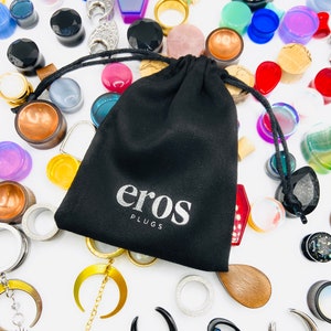 May include: A black velvet pouch with the words "eros plugs" printed in white. The pouch is surrounded by a variety of colourful and patterned ear gauges.