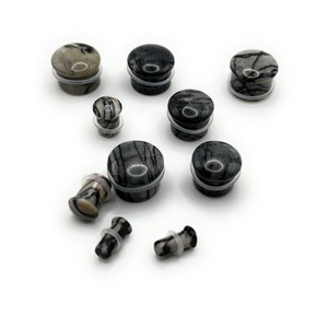 May include: A set of eight black and white striped stone ear gauges of various sizes. The gauges are made of natural stone and have a smooth, polished finish.