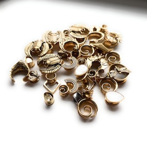 May include: A collection of gold-colored ear gauges in various designs, including scarabs, spirals, and geometric shapes. Some gauges feature white, teardrop-shaped inlays. The gauges are scattered on a white surface, showcasing their intricate details.