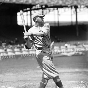 May include: A baseball player in a uniform swings a wooden bat at a baseball. The player is wearing a cap and has a determined expression on their face.