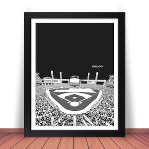 May include: Black and white framed print of a baseball stadium, with the word "Chicago" at the top. The stadium is filled with spectators, and the field is in the foreground. The print is displayed on a wooden surface.