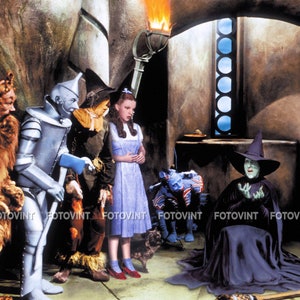 May include: A scene from the movie The Wizard of Oz. Dorothy in a blue dress and red shoes stands with the Tin Man, Scarecrow, and Cowardly Lion. The Wicked Witch of the West is seated, and a small dog is present.