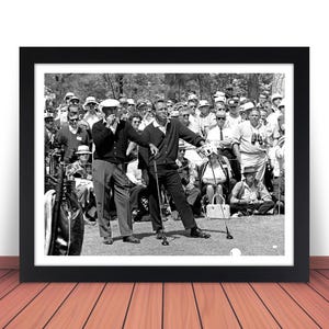 May include: Black and white photograph of two men playing golf. The men are wearing golf attire and are standing on a green golf course. There are spectators in the background.