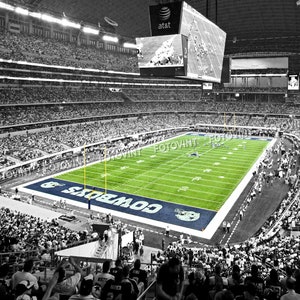 May include: A black and white aerial view of a football stadium with a green field and a large scoreboard displaying the word "at&t". The field is marked with the words "Cowboys" in blue and white.