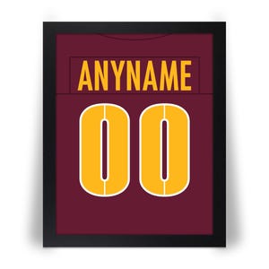 May include: Framed burgundy jersey with the text "ANYNAME" in gold letters above the number "00". The numbers are gold with a white outline. The jersey is framed in a black frame.