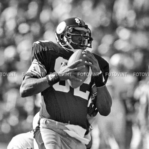 May include: A black and white photo of a football player wearing a jersey with the number 82 on it. The player is holding a football and is looking down at it.