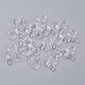 May include: A pile of clear plastic clips with small round balls on the ends. The clips are designed to hold items together.