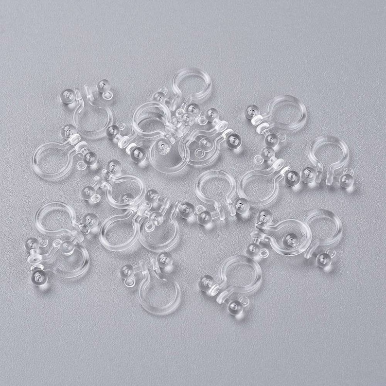 May include: A pile of clear plastic clips with small round balls on the ends. The clips are designed to hold items together.