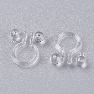 May include: Two pairs of clear plastic earring backs. Each back has a small, clear plastic ball on one end and a loop on the other end.