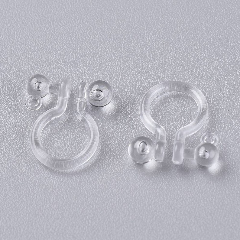 May include: Two pairs of clear plastic earring backs. Each back has a small, clear plastic ball on one end and a loop on the other end.