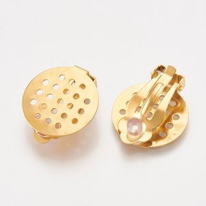 K&ouml;nnte beinhalten: Ein Paar goldfarbene Ohrclips mit rundem, perforiertem Design. Ein Ohrclip hat einen kleinen rosa Stein in der Mitte.