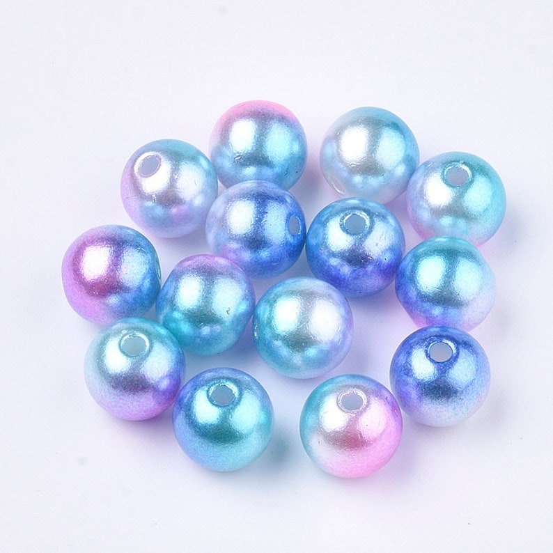 May include: A group of iridescent blue, pink, and purple round beads. The beads have a pearlescent finish and are perfect for crafting.