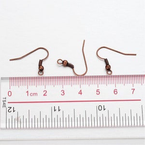 May include: Three copper-colored earring hooks with a small ball at the end of each hook. The hooks are measured against a ruler with markings in centimeters.