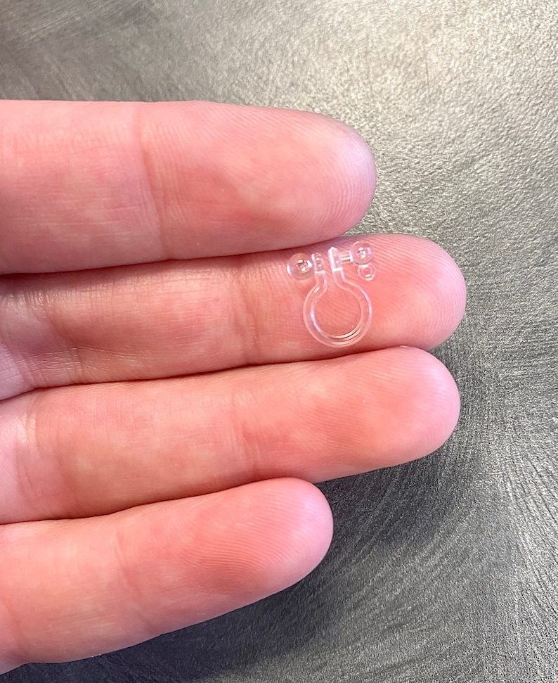 May include: Clear plastic ring with two small bumps on each side. The ring is designed to hold a curtain or other fabric in place.