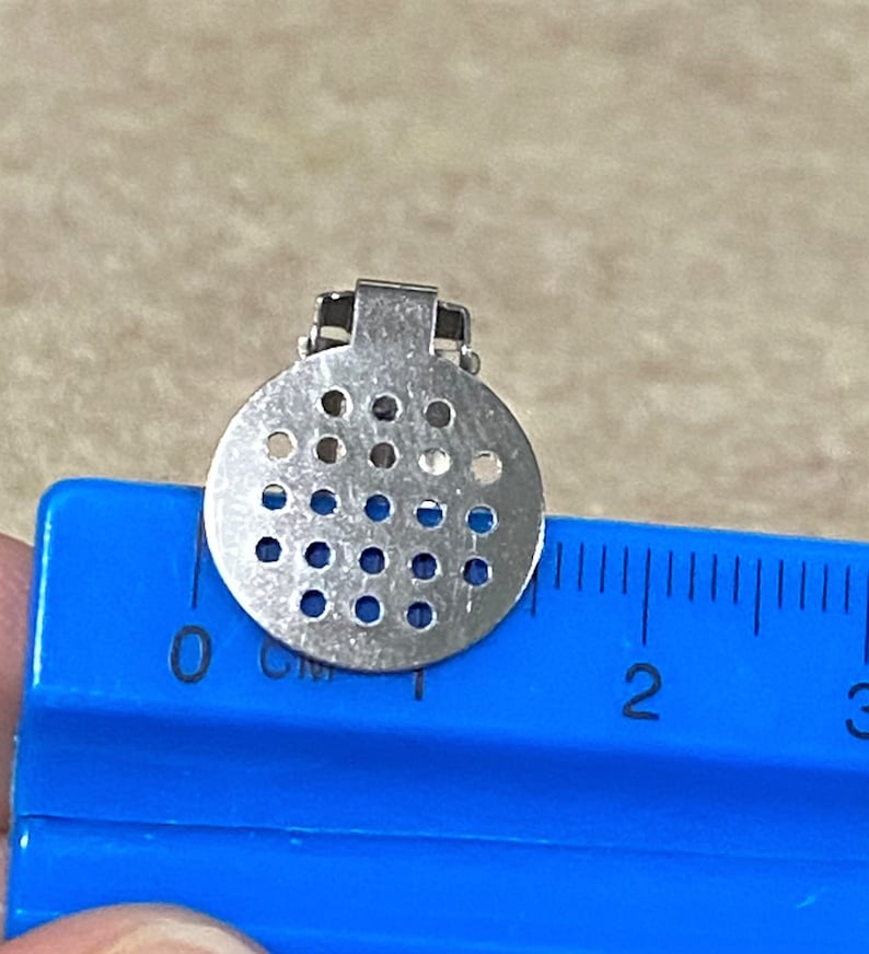 K&ouml;nnte beinhalten: Eine silberfarbene Metall-Filterplatte mit einem Durchmesser von etwa 2,5 cm. Die Filterplatte hat eine runde Form und ist mit einem Gittermuster aus kleinen L&ouml;chern versehen.